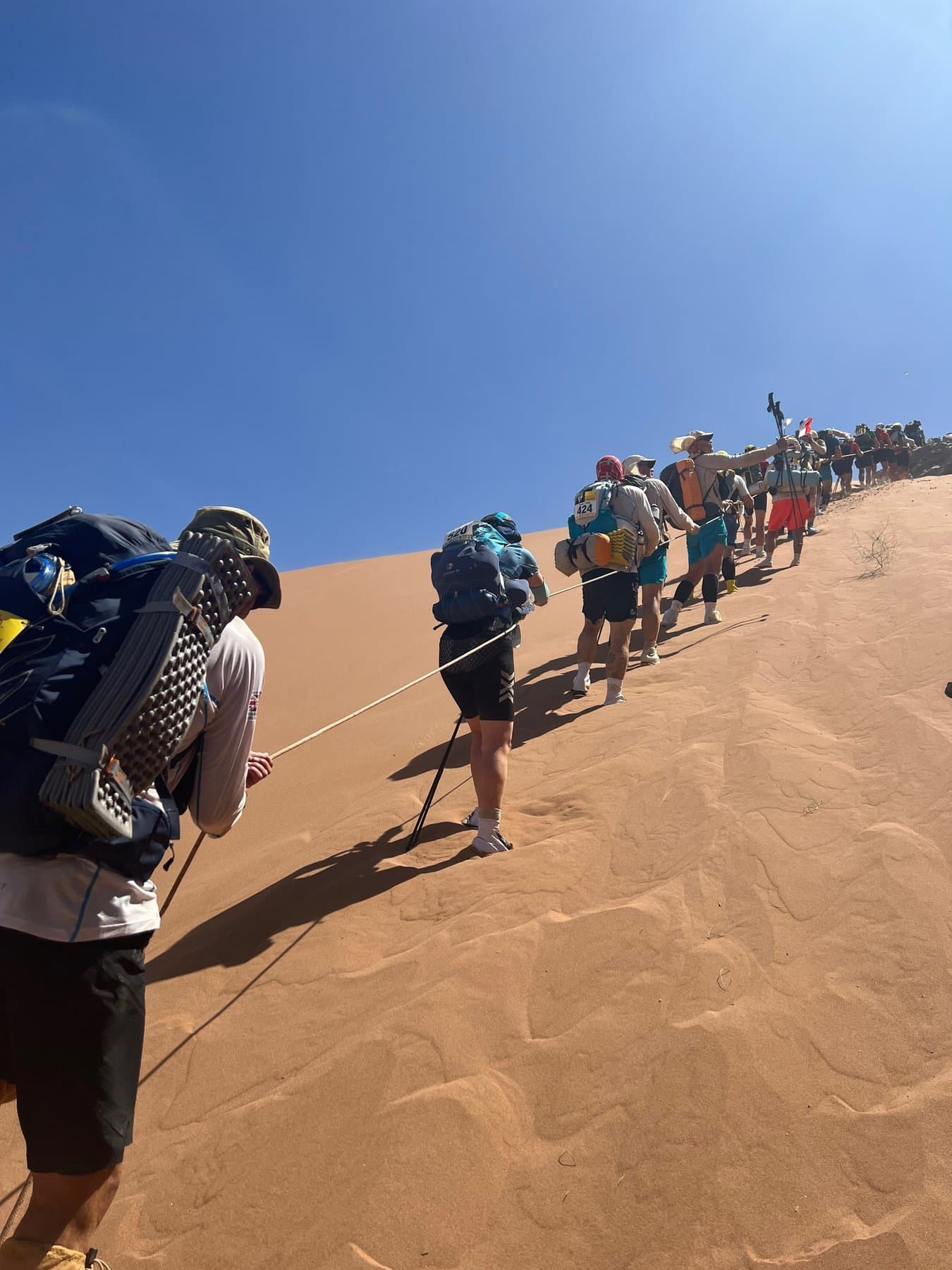 Line of runners hauling themselves up a huge sand dune on a fixed rope