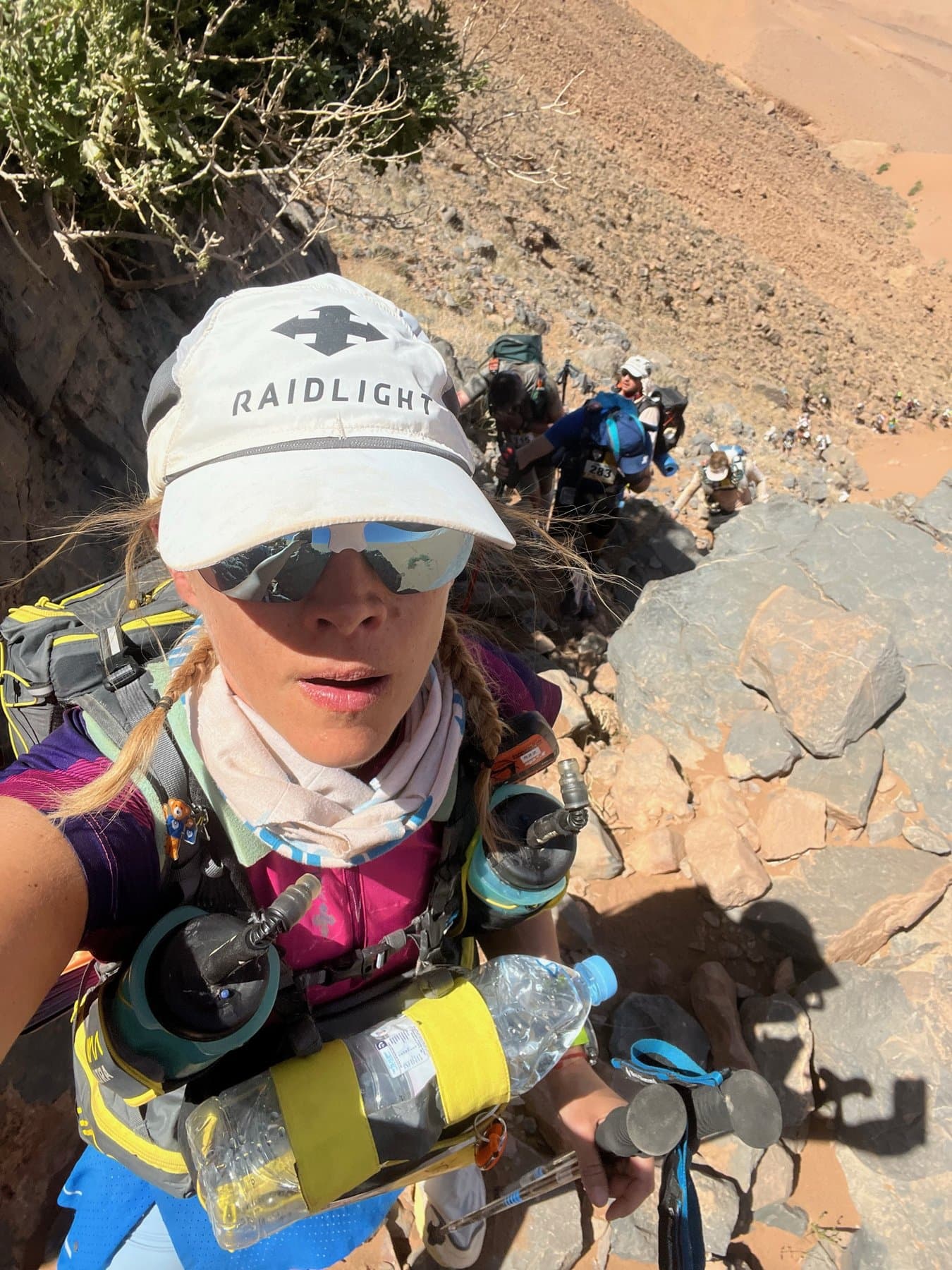 Charlotte scrambling up a rocky slope to the ridge with runners behind her