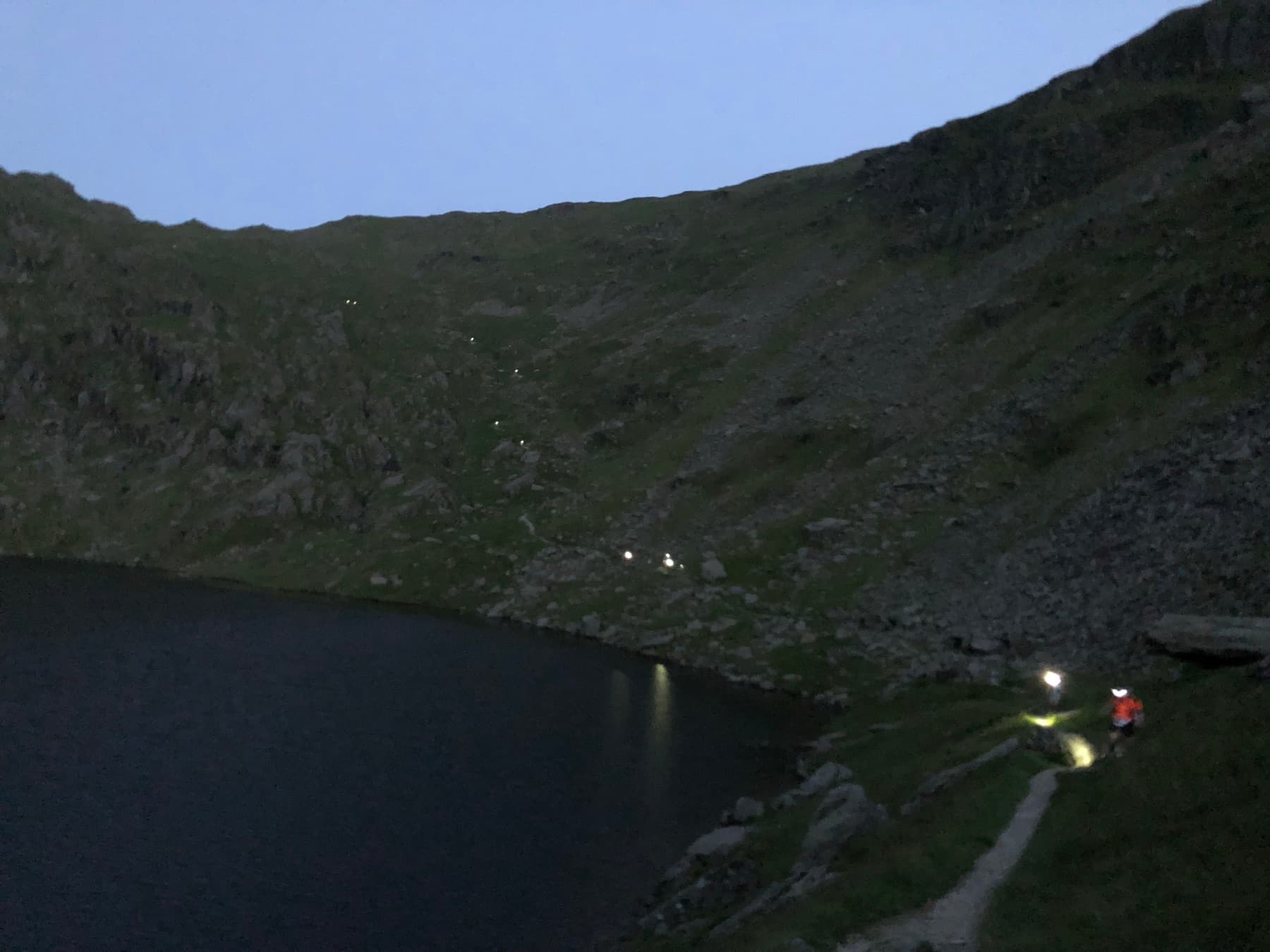 Runners with head torches descending the pass beside Small Water at dusk