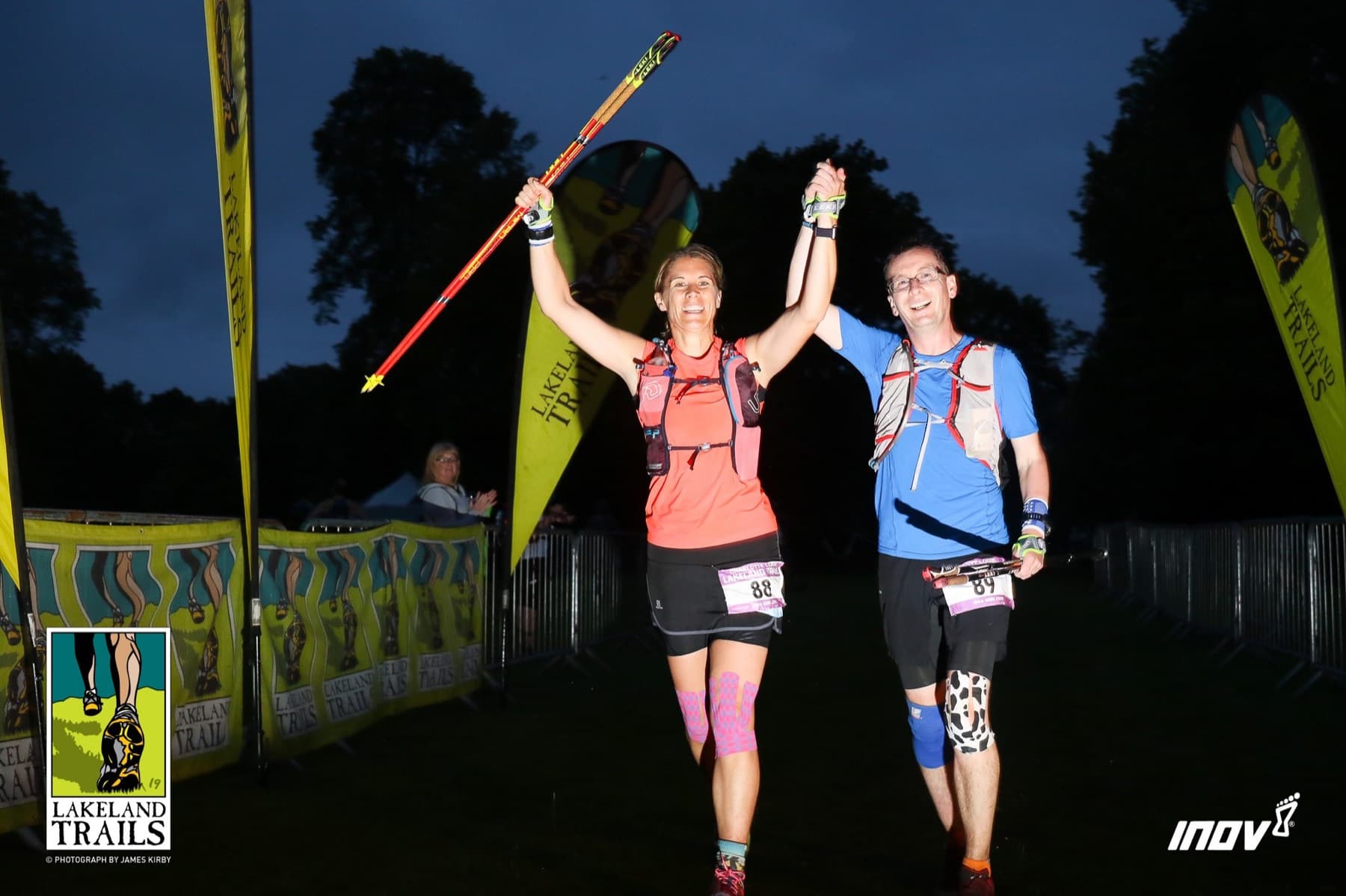 Runner and Scott raising arms as they cross the Lakeland Trails 100km finish line at night