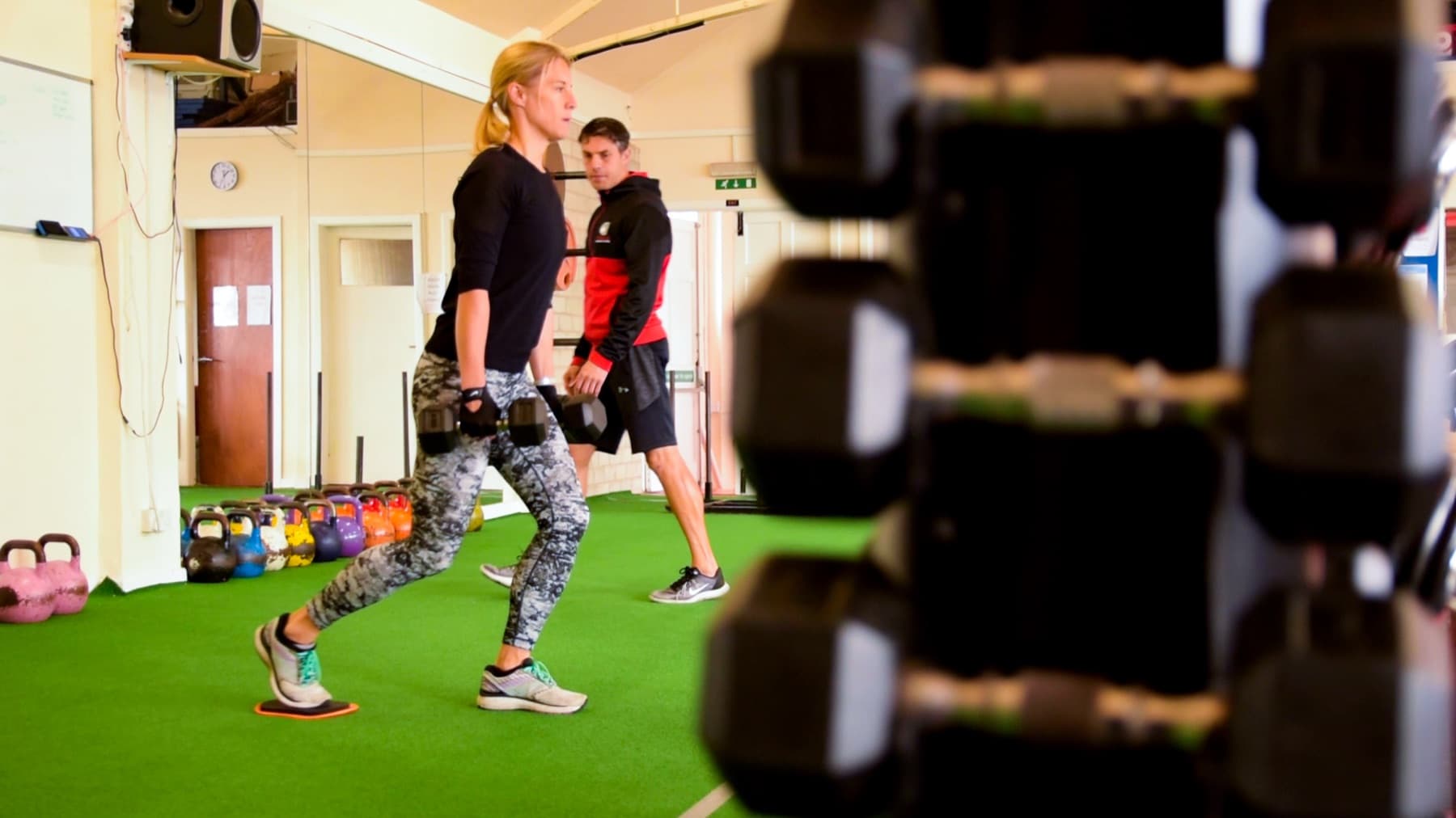 Client performing dumbbell lunges on the turf with a trainer watching