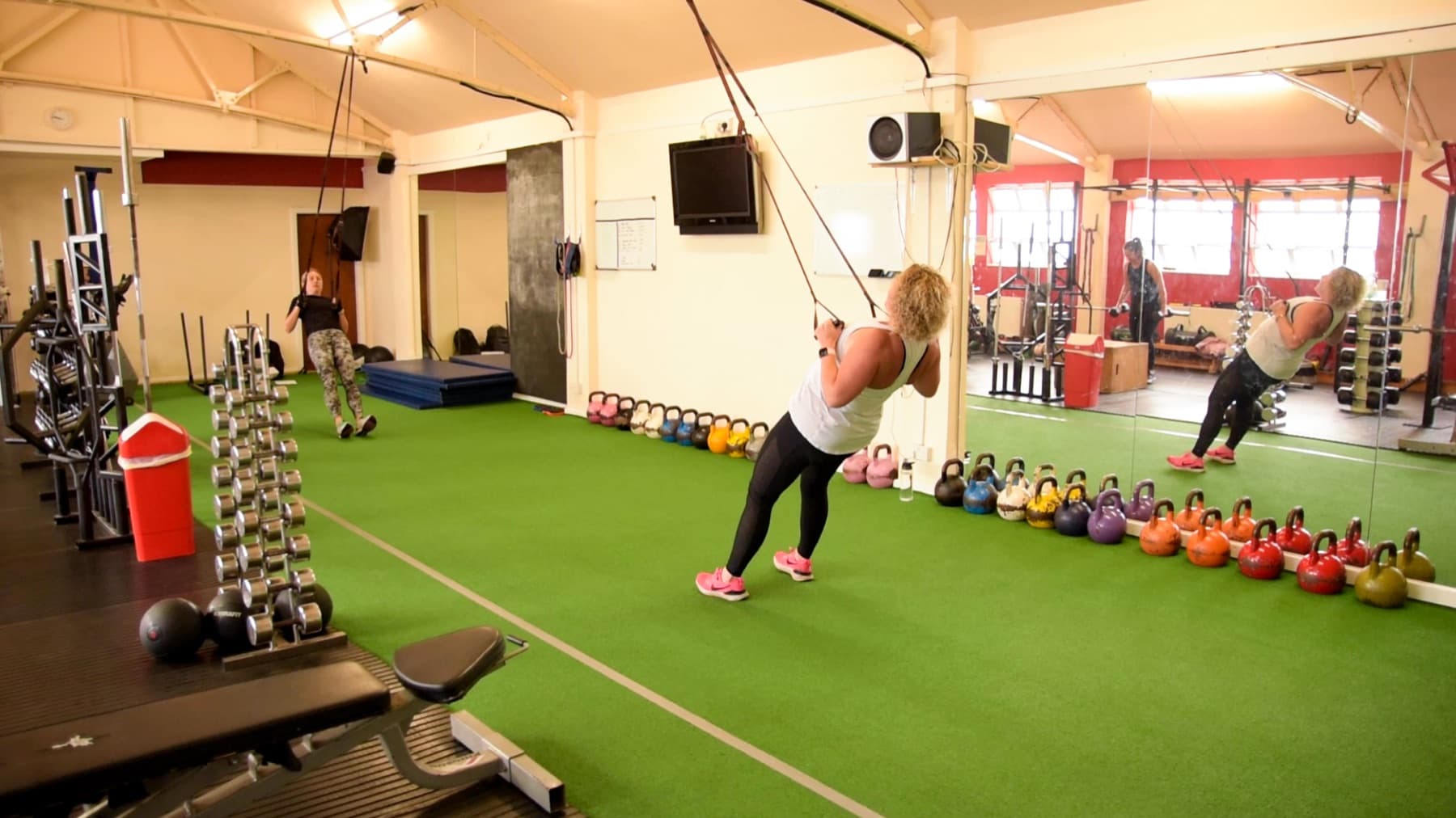Client performing suspension trainer rows beside the kettlebell rack
