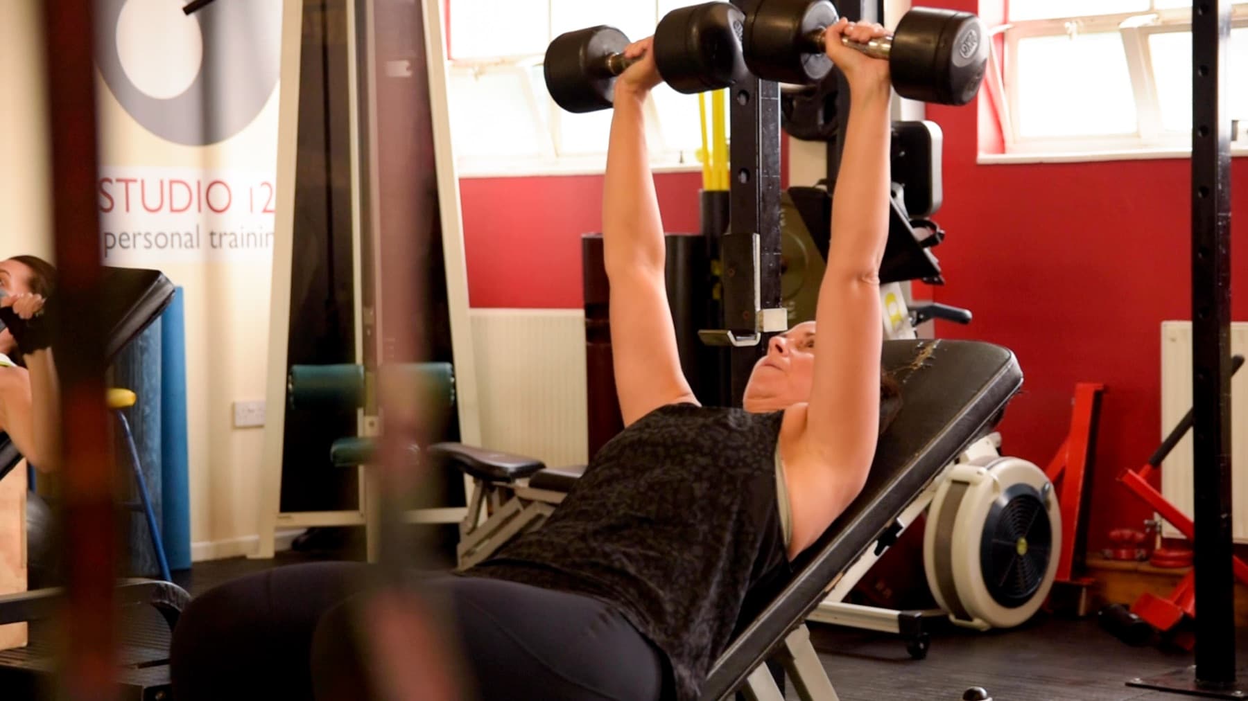 Client pressing dumbbells on an incline bench beside the Studio 121 banner